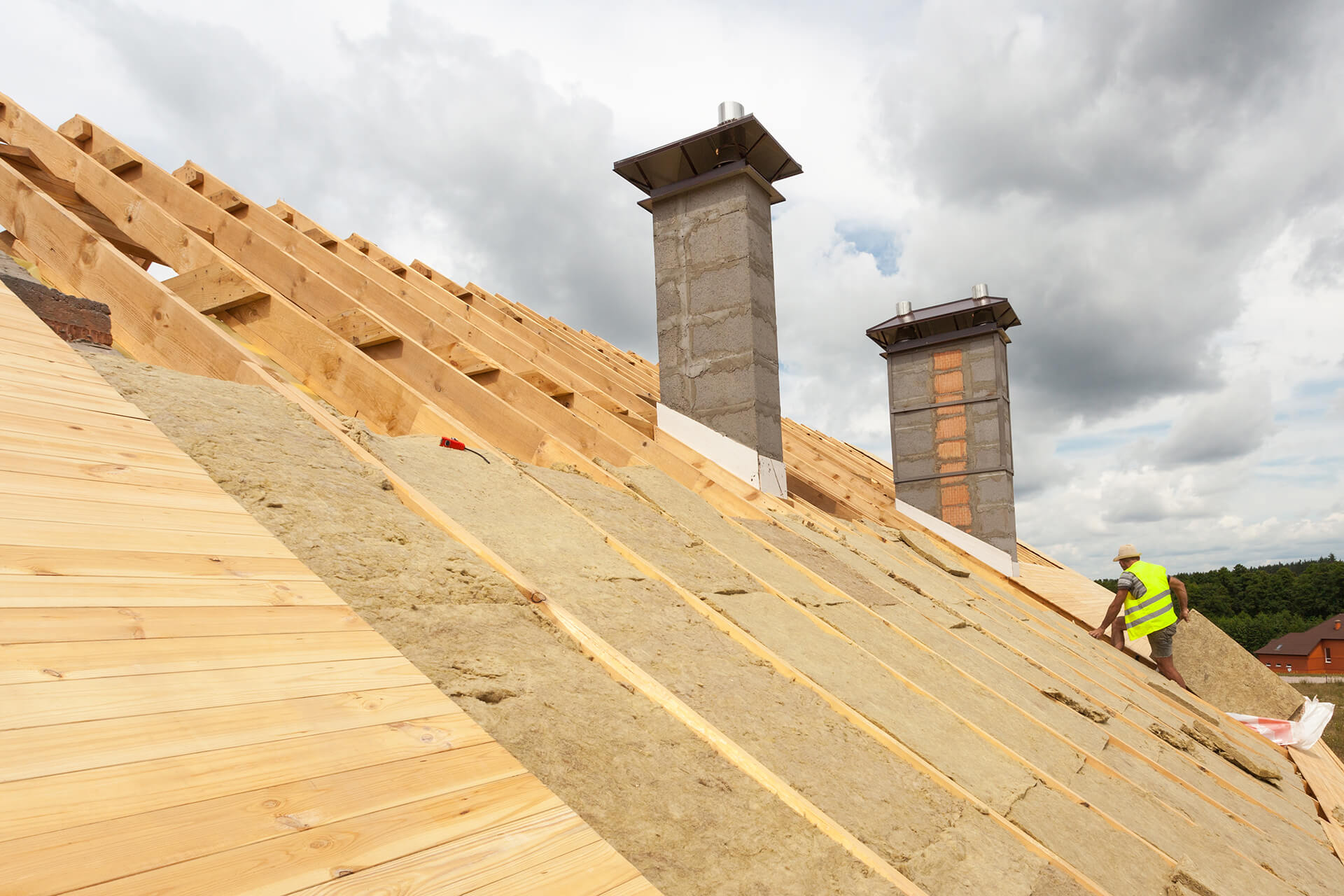Ein Handwerker in gelber Weste, der Dämmung auf einem Dach anbringt – symbolische Darstellung für die Sanierung bzw. die Dämmung eines Dachs mit der Wüstenrot Energieberatung