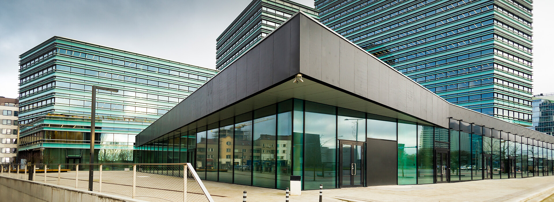 Ein moderner gewerblicher Häuserkomplex mit Glasfronten und mehreren (Hoch-)Häusern - symbolische Darstellung des förderfähigen energetischen Sanierungskonzeptes für Nichtwohngebäude gemäß DIN V 18599 durch die Wüstenrot Energieberatung