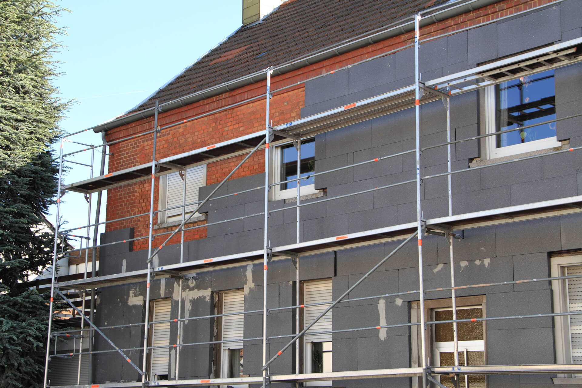 Ein Haus mit roten Ziegeln, an welchem ein Baugerüst und zum Teil bereits Fassadendämmung angebracht ist – symbolische Darstellung für die Fassadendämmung mit der Wüstenrot Energieberatung