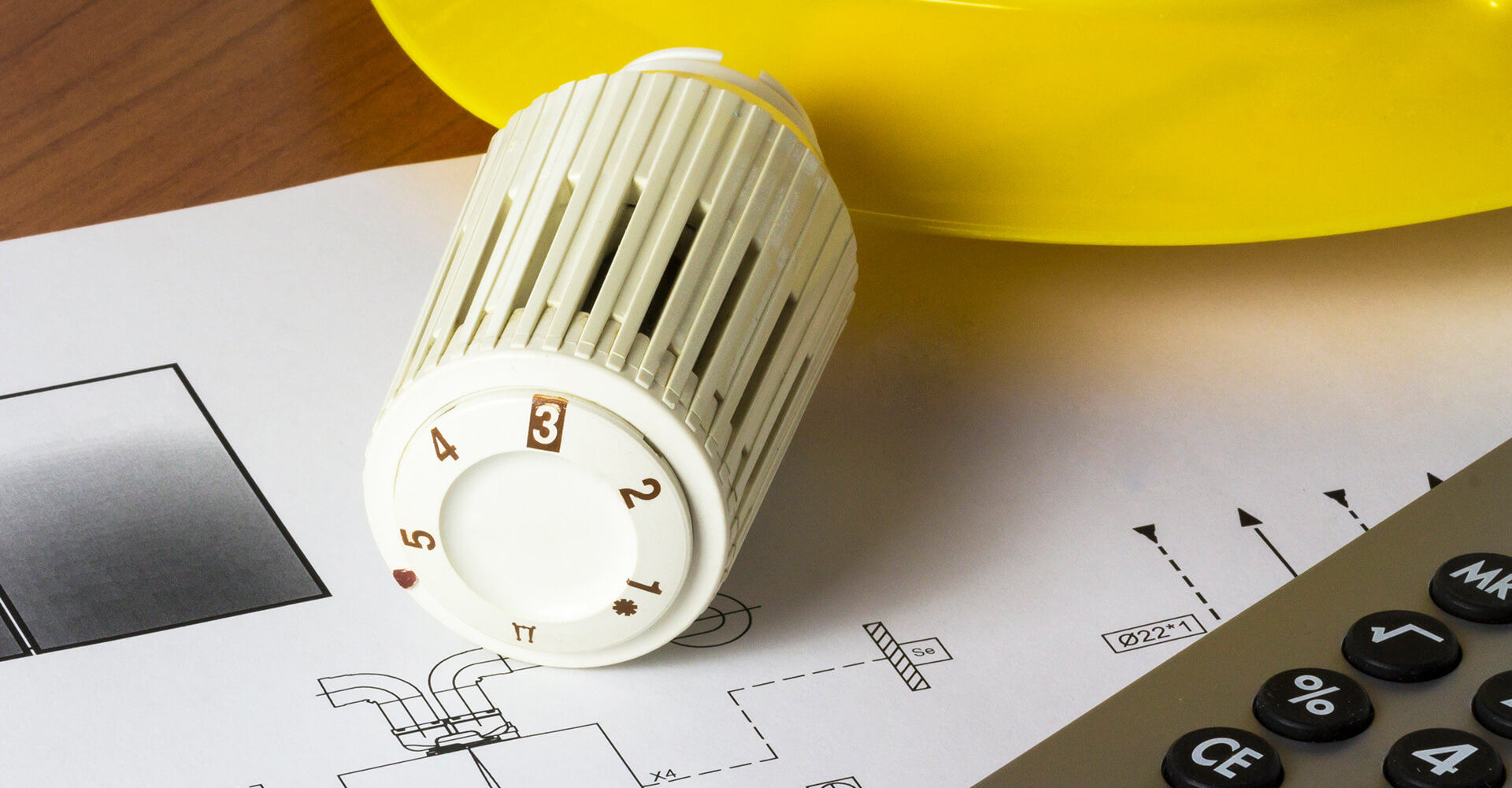 Ein Heizungsthermostat, Pläne und mehr auf einem Schreibtisch – symbolische Darstellung für die Heizlastberechnung und den hydraulischen Abgleich durch die Wüstenrot Energieberatung