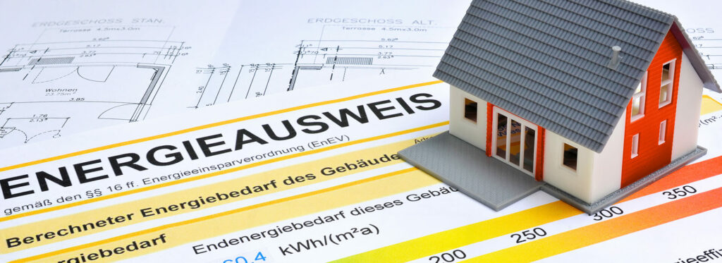 Ein Energieausweis, ein Grundriss und ein kleines Haus auf einem Schreibtisch – symbolische Darstellung für Online-Energieausweise der Wüstenrot Energieberatung